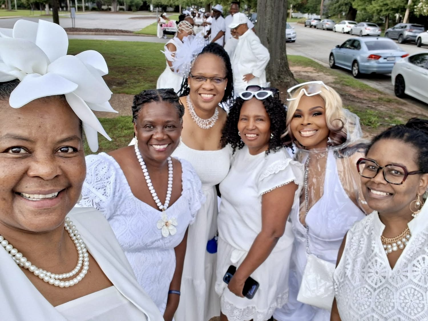 Sorors dressed in white gathered outdoors before a community service procession